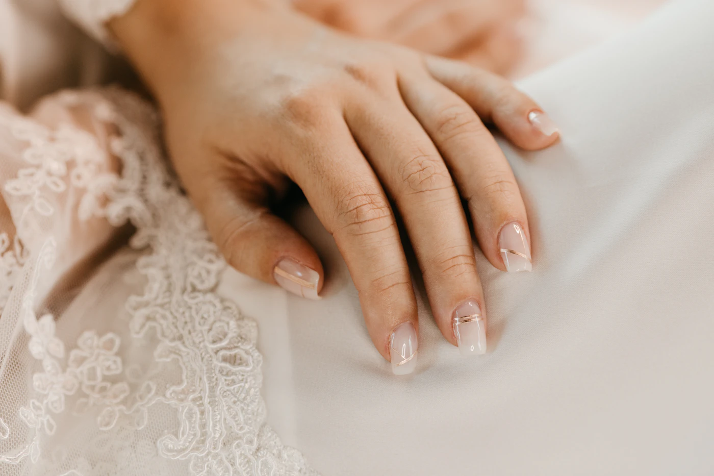 Dłonie panny młodej z delikatnym manicure na tle koronki