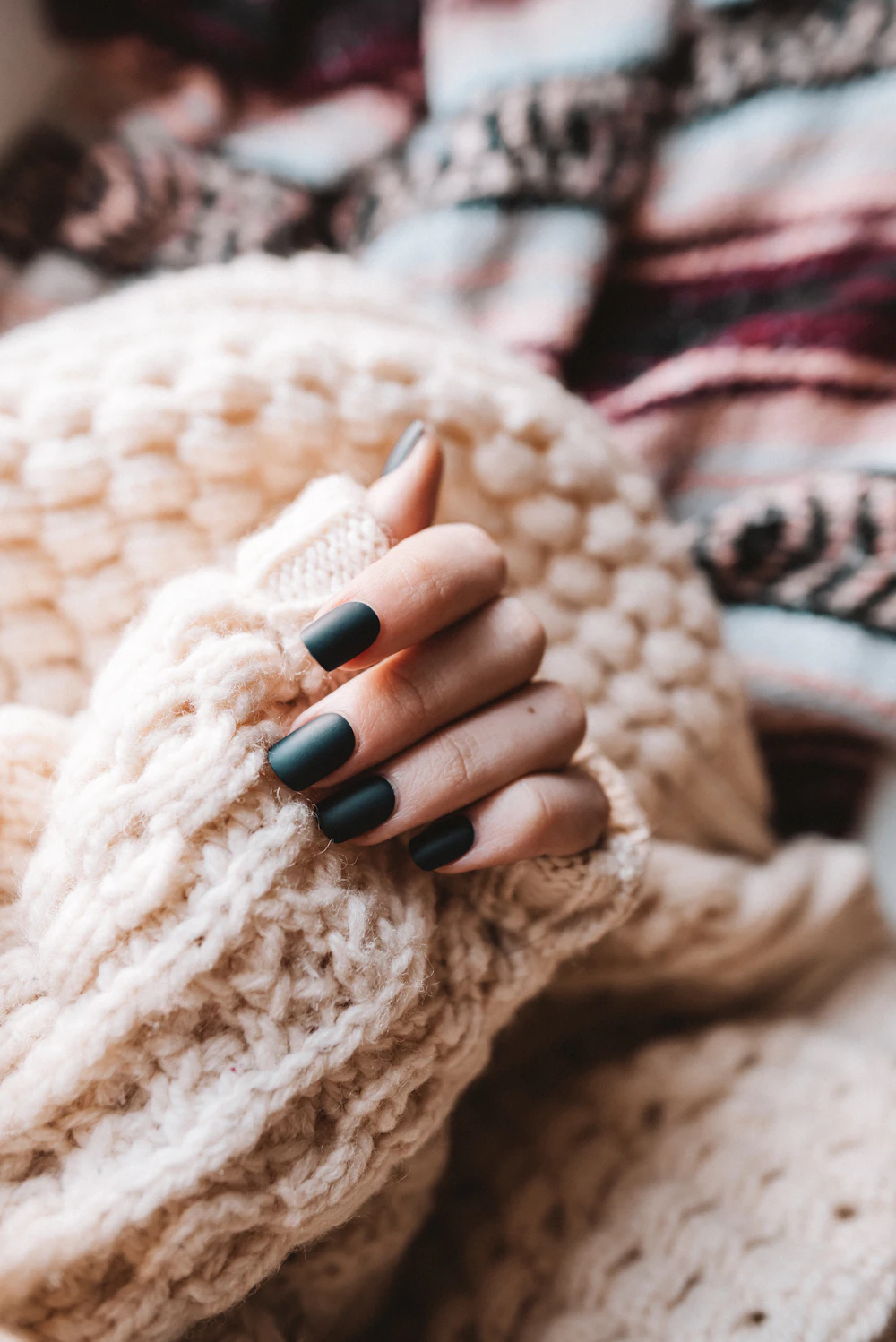Dłonie z ciemnym manicure otulone kremowym swetrem